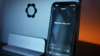 Phone leaning against a silver computer. the screen of the phone shows the ChatGPT landing page 